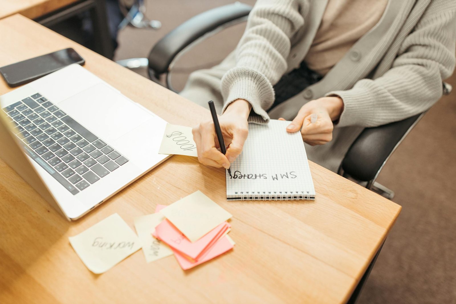 Adult writing notes in a notebook at a desk with a laptop, emphasizing productivity.